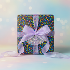 Square gift wrapped in colorful confetti wrapping paper with sheer lavender ribbon and "Sweet Surprises" tag.
