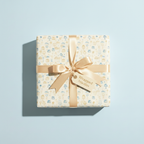 Square gift wrapped in birthday wrapping paper with cakes and a gold satin ribbon.