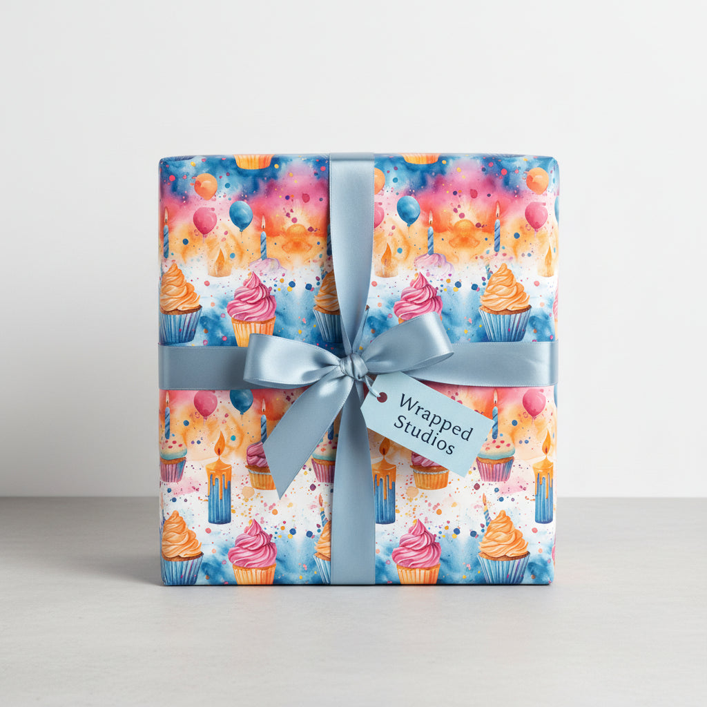 Square gift wrapped in watercolor birthday wrapping paper with cupcakes, balloons, and a blue ribbon.