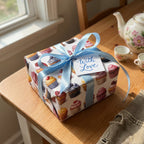 Whimsical cupcake wrapping paper, tied with a blue satin ribbon and "With Love" tag, perfect for a birthday or special occasion.
