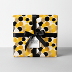 Modern polka dot wrapping paper in black, white, and yellow with a black ribbon bow and "Wrapped Studios" gift tag, ideal for birthday or luxury gifts.