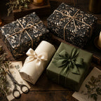 Dark floral wrapping paper and green luxury gift wrap with silk ribbons by Wrapped Studios on a rustic table.