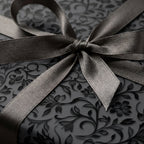 Elegant floral wrapping paper in dark gray with a satin ribbon bow, from Wrapped Studios.