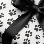 Dog paw print wrapping paper with a black satin bow on a gift box by Wrapped Studios.