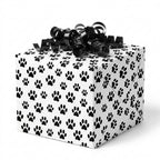 Black and white dog paw print wrapping paper on a gift box with a black curly bow by Wrapped Studios.