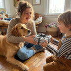 Child receiving a gift in black dog paw print wrapping paper from a woman and golden retriever. Wrapped Studios.