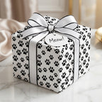 Black and white paw print wrapping paper on a gift box with a white ribbon and Meow tag, by Wrapped Studios.