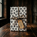 Dog paw print wrapping paper with rustic twine bow and gift tag on wood table by Wrapped Studios.
