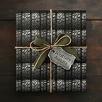 Fun wrapping paper featuring a pattern of tires, tied with jute and a green ribbon, gift tag reads "Journey Awaits."