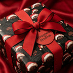 Black Santa Christmas wrapping paper with a red bow and tag by Wrapped Studios.