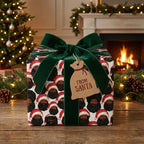 Black Santa wrapping paper with a green velvet bow by Wrapped Studios, in front of a Christmas fireplace.