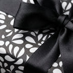 Elegant black and white patterned gift wrap with a modern abstract design and a luxurious black satin ribbon bow.
