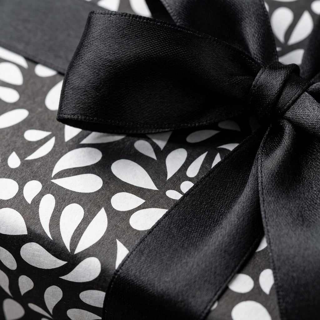 Elegant black and white patterned gift wrap with a modern abstract design and a luxurious black satin ribbon bow.
