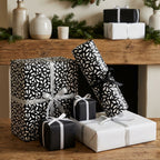 Elegant black and white teardrop wrapping paper and solid boxes with silver and black ribbons on a rustic holiday mantel.