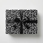Elegant black and white wrapping paper with an abstract leaf pattern and a black satin bow on a rectangular gift box.