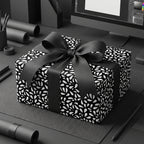 Luxury black gift wrap featuring a modern white leaf pattern and a large black ribbon bow on a present.