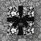 Elegant square gift wrapped in black floral wrapping paper with a black velvet bow.