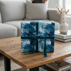 Square gift wrapped in blue abstract art paper with a green velvet ribbon on a rustic wood table.