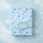 Light blue baby shower wrapping paper with gift and balloon pattern, tied with white ribbon and "Sweetest Wishes" tag.