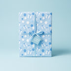 Light blue birthday wrapping paper with balloon and gift pattern, tied with ribbon and tag.