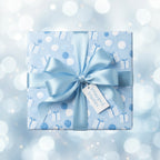 Light blue birthday wrapping paper with gift and balloon pattern, tied with satin ribbon on a bokeh background.