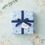 Light blue birthday wrapping paper with presents and balloons, tied with a navy ribbon bow.