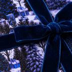 Luxury Christmas wrapping paper with winter forest pattern and blue velvet bow by Wrapped Studios.