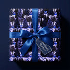 Blue Christmas wrapping paper featuring a winter forest pattern and satin bow, by Wrapped Studios.