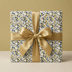 Luxury gift box featuring navy, gold, and white abstract confetti wrapping paper with a classic gold satin ribbon.