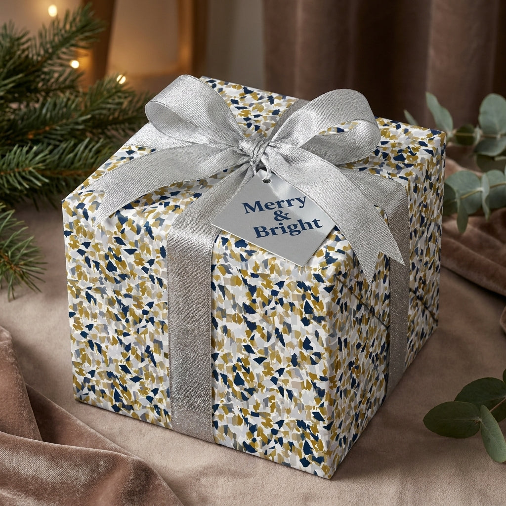 Gift box with blue and gold terrazzo Christmas wrapping paper, tied with a silver ribbon and Merry & Bright tag.