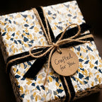 Luxury gift box wrapped in modern blue and gold terrazzo paper with a black velvet ribbon and rustic twine tag.