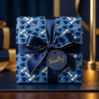Blue graduation wrapping paper with caps and diplomas, tied with a navy ribbon by Wrapped Studios.