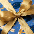 Blue graduation wrapping paper with caps, diplomas, and a gold ribbon bow by Wrapped Studios.
