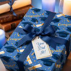 Blue graduation wrapping paper with cap pattern, navy ribbon, and gift tag by Wrapped Studios.