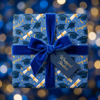 Blue and gold graduation wrapping paper with caps, diplomas, and a velvet bow by Wrapped Studios.