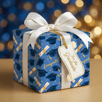 Blue graduation wrapping paper with caps, scrolls, and a white satin bow, by Wrapped Studios.