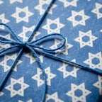 Hanukkah wrapping paper with a white Star of David pattern and blue twine bow by Wrapped Studios.