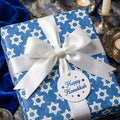 Elegant blue Hanukkah wrapping paper with Star of David print and white satin bow by Wrapped Studios.