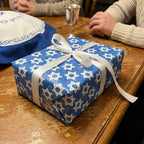 Blue Hanukkah wrapping paper with Star of David pattern and white ribbon by Wrapped Studios.