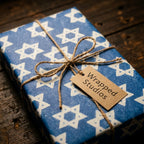 Blue Star of David Hanukkah wrapping paper on a gift box tied with rustic twine by Wrapped Studios.