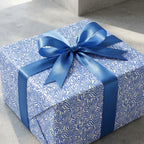 Modern blue and white wavy pattern wrapping paper on a square gift box tied with a large blue satin ribbon bow.