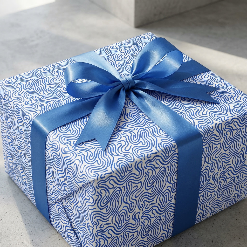 Modern blue and white wavy pattern wrapping paper on a square gift box tied with a large blue satin ribbon bow.