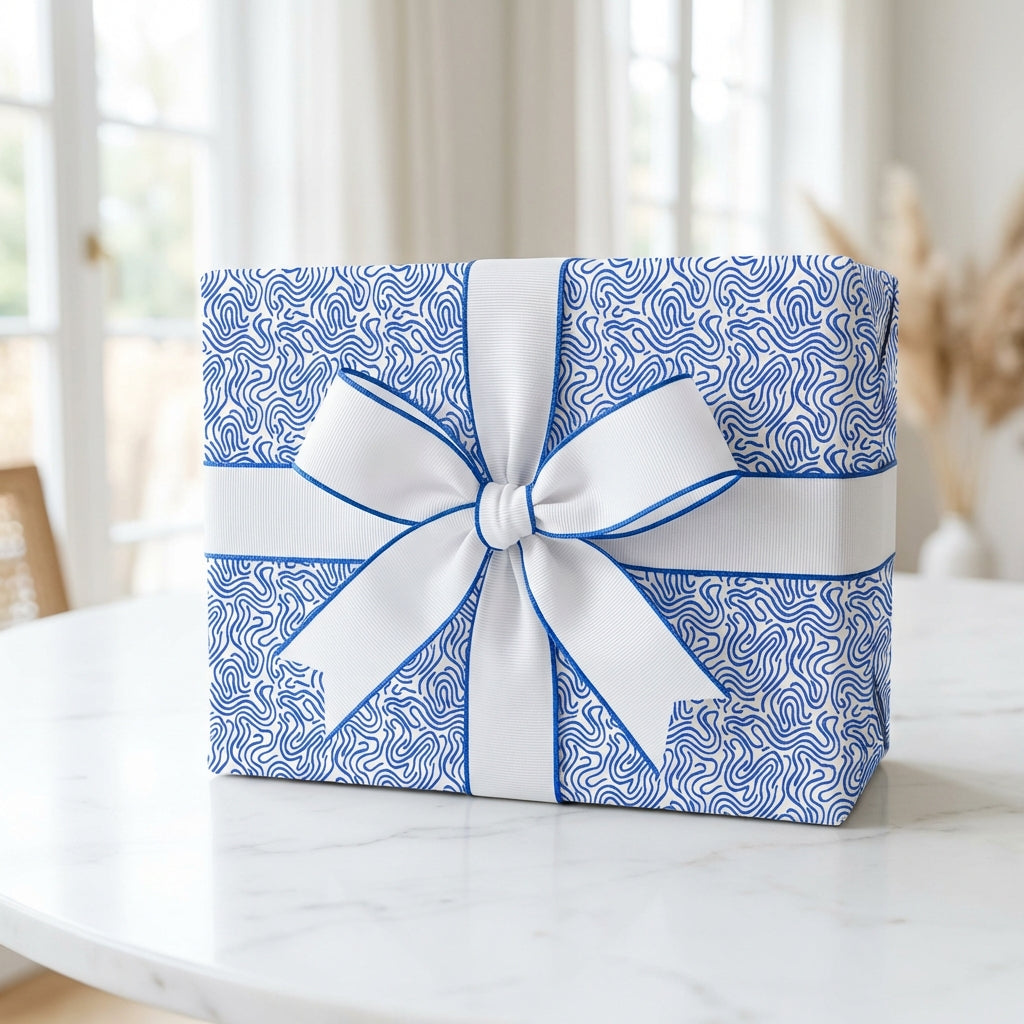 Modern blue and white abstract patterned gift wrap with a white grosgrain ribbon bow and blue trim, sitting on a marble table.