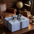 Sophisticated blue abstract swirl wrapping paper with a grey ribbon bow, shown on a wooden desk in a study.