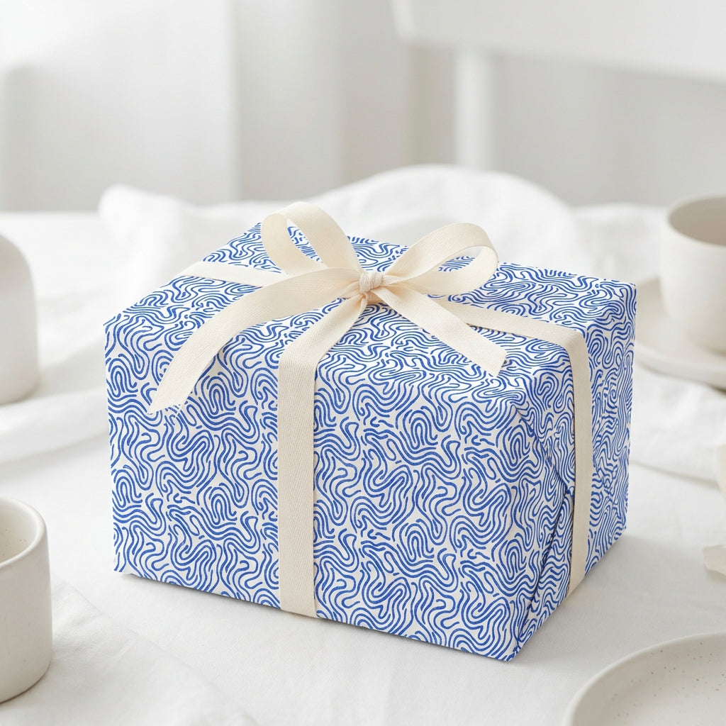 Elegant blue and white wavy pattern gift wrap with a cream ribbon bow, perfect for modern birthday or wedding presents.