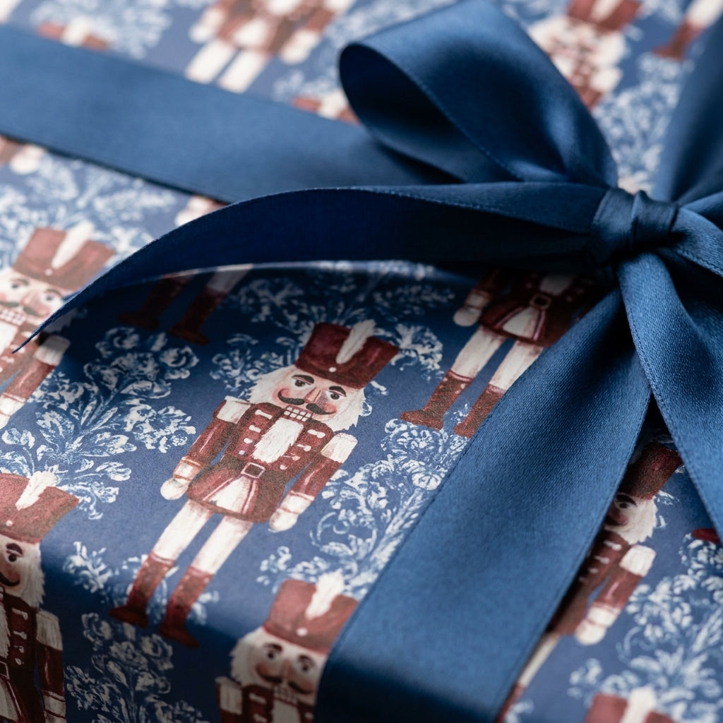 Navy blue nutcracker Christmas wrapping paper with a satin ribbon bow by Wrapped Studios.