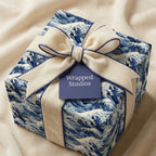 Square gift wrapped in blue wave-patterned paper with a cream velvet ribbon and dark blue trim.