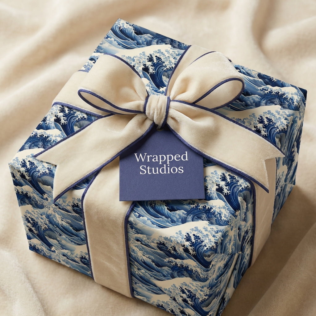 Square gift wrapped in blue wave-patterned paper with a cream velvet ribbon and dark blue trim.