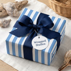 Blue striped nautical wrapping paper with a navy bow and coastal seashells by Wrapped Studios.