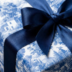 Blue and white toile wrapping paper with a navy satin bow on a luxury gift box by Wrapped Studios.